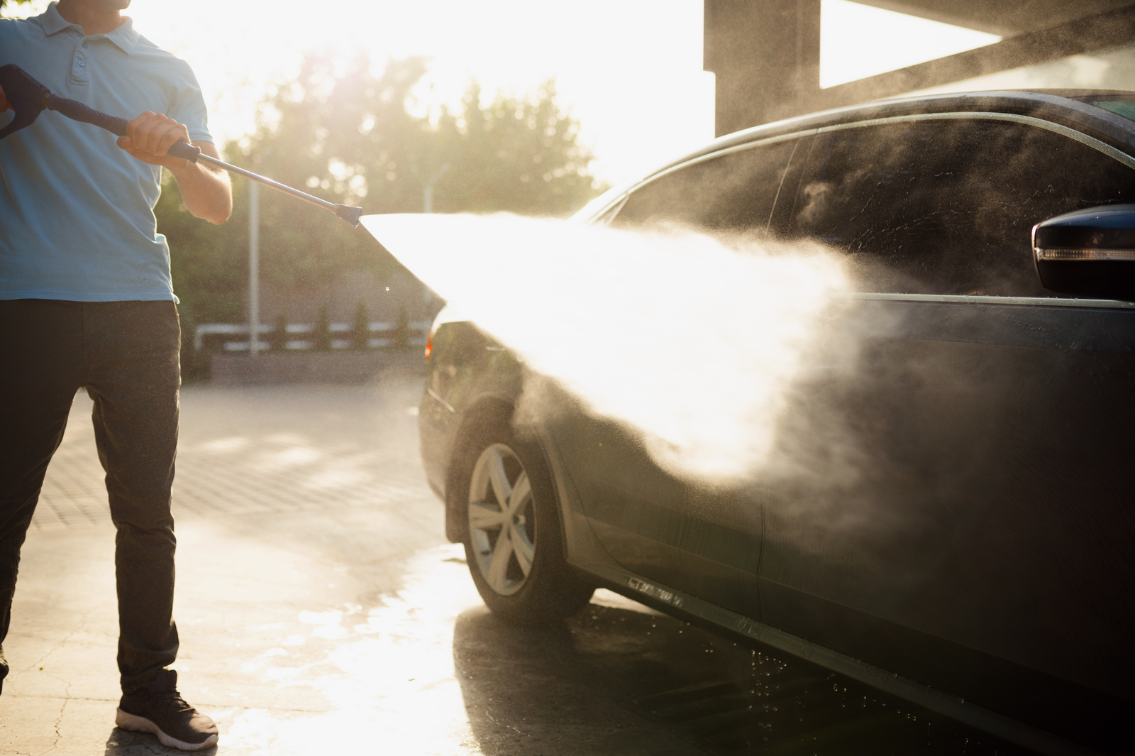 Man holds high pressure water gun, car wash station. Carwash industry or business. Male person cleans his vehicle